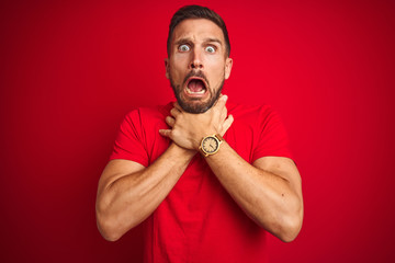 Wall Mural - Young handsome man wearing casual t-shirt over red isolated background shouting suffocate because painful strangle. Health problem. Asphyxiate and suicide concept.