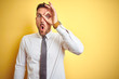 © Krakenimages.com - Young handsome business man wearing elegant white shirt over yellow isolated background doing ok gesture shocked with surprised face, eye looking through fingers. Unbelieving expression.