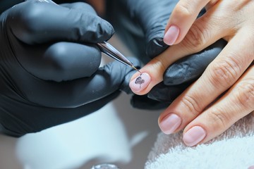 Close-up beautician painting art design on nails.