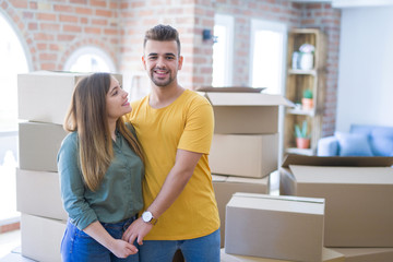 Wall Mural - Young beautiful couple in love around cardboard boxes moving to new home, smiling very happy and cheerful for new apartment