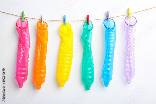 Fotografía Used colorful condoms hanging on clothesline against white background