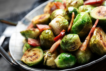 Delicious Brussels sprouts with bacon in dish on table, closeup