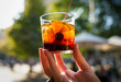 © Gypsy Picture Show - This image capture shows a hand holding a glass of refreshing vermouth alcoholic beverage in outdoors in the sunlight