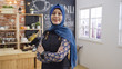 © PRPicturesProduction - portrait of attractive asian muslim female cafe startup business owner standing crossed arm in coffee shop. malay entrepreneur concept. young woman in headset face camera smiling in coffeehouse.