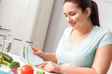 Body Care. Chubby girl sitting at kitchen table reading meal plan smiling cheerful side view close-up