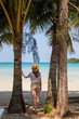 © allenkayaa - A young woman under a palm tree on the shore of the Gulf of Thailand. Woman in a hat looks at the sea
