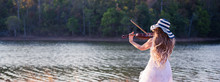 Violinist Woman Wearing White Dress With Hat Playing Violin At Lakeside