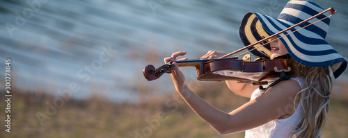 Fototapeta skrzypce  skrzypaczka-ubrana-w-biala-sukienke-z-kapeluszem-grajaca-na-skrzypcach-nad-jeziorem
