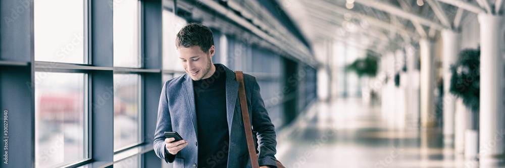 Business man texting on mobile phone at airport on business trip using cellphone texting sms message on smartphone app - young businessman commuter lifestyle panoramic banner. - obrazy, fototapety, plakaty 