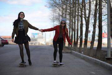  A young hipster girl is riding a skateboard. Girls girlfriends for a walk in the city with a skateboard. Spring sports on the street with a skateboard.