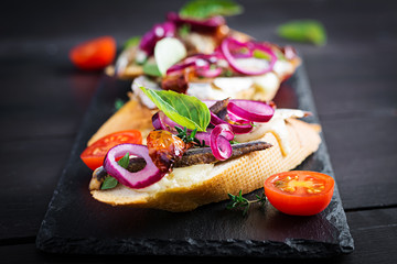 Tapas - Spanish bar food. Bruschetta with slices of sun-dried tomatoes,cheese mozzarella and anchovies on dark background.