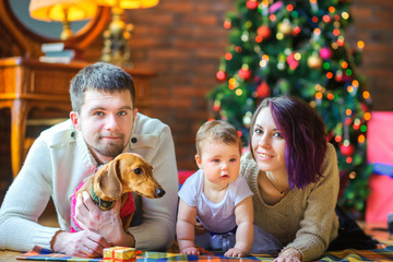 Happy family with a puppy lie on the floor near the festive Christmas tree. Holidays