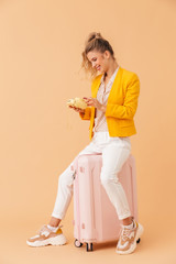 Poster - Photo of smiling woman using retro camera while sitting on suitcase