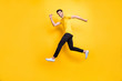 © deagreez - Full length photo of handsome guy jumping high speed running competition participant rushing shopping wear casual t-shirt black trousers isolated yellow color background