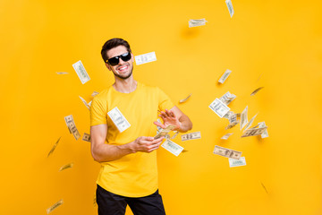 Poster - Photo of young handsome careless guy throwing usa money banknotes away wealthy person wear sun specs casual t-shirt isolated bright yellow color background