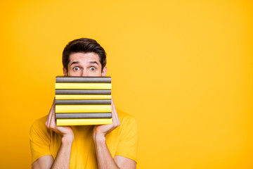 Poster - Close-up portrait of his he nice attractive funny brunette guy holding in hands hiding behind pile of book scary difficult knowledge isolated over bright vivid shine vibrant yellow color background