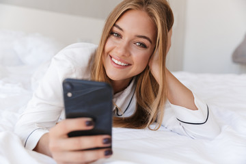 Sticker - Photo of cheerful woman using cellphone and smiling while lying on bed