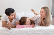 Happy family, including father mother and daughter, are lying down on bed with smile, looking at each other