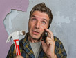 © TheVisualsYouNeed - funny portrait of messy and frustrated man calling domestic insurance on mobile phone for repair mess he did with a hammer cracking the wall needing professional help
