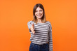 © khosrork - Portrait of friendly young woman with brown hair in long sleeve striped shirt standing, stretching hand for handshake, smiling at camera, offering cooperation. indoor studio shot isolated on orange