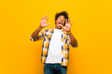Wall Mural - young black man feeling stupefied and scared, fearing something frightening, with hands open up front saying stay away against orange wall
