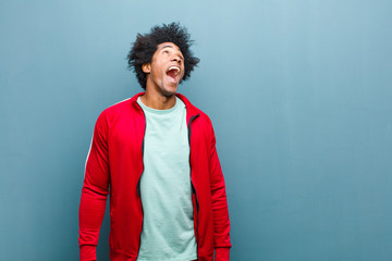 Wall Mural - young black sports man screaming furiously, shouting aggressively, looking stressed and angry against grunge wall