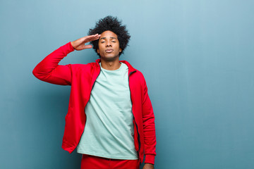 Wall Mural - young black sports man greeting the camera with a military salute in an act of honor and patriotism, showing respect against grunge wall