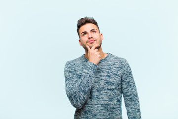 Wall Mural - young hispanic man thinking, feeling doubtful and confused, with different options, wondering which decision to make against blue background