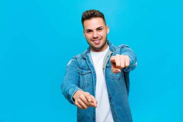 Wall Mural - young hispanic man feeling happy and confident, pointing to camera with both hands and laughing, choosing you against blue background