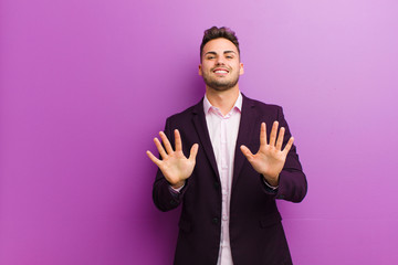 Wall Mural - young hispanic man smiling and looking friendly, showing number ten or tenth with hand forward, counting down