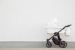 New, white baby stroller on pavement. Empty place for text, quote or sayings on light gray wall background.