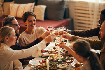 Poster - High angle view at elegant young people clinking champagne glasses while enjoying Christmas dinner at home, copy space