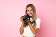 © luismolinero - Young blonde woman over isolated pink background with a professional camera