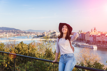 Wall Mural - A happy young woman enjoying her trip to Budapest, Hungary from the point from Gellert Hill during sunrise in autumn during sunrise.