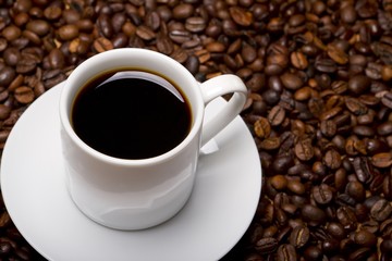 Poster - High angle shot of a white cup of black coffee on a surface full of coffee beans