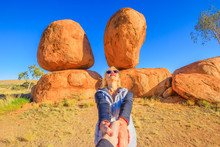 Couple Hand In Hand At Iconic Devils Marbles In Northern Territory: The Eggs Of Mythical Rainbow Serpent. Follow Me, Tourist Woman At Outback Landscape, One Of Australia's Most Famous Natural Wonders.
