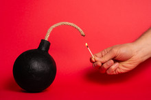 Photo Of A Round Bomb With Lit Fuse On A Red Background. Bomb And Match.