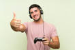 © luismolinero - Young handsome man playing with a video game controller over isolated green wall with thumbs up because something good has happened