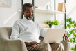 © LIGHTFIELD STUDIOS - Smiling African American man sitting in armchair and using laptop