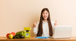 © Asier - Young nutritionist chinese woman working with her laptop indicates with both fore fingers up showing a blank space.