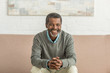 © LIGHTFIELD STUDIOS - senior african american man sitting on sofa with clenched hands and smiling at camera