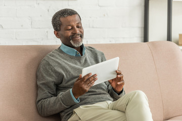 smiling african anerican man using laptop while sitting on sofa