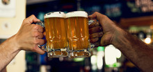 Close-up Of Hands Toasting Beer Mugs In The Bar