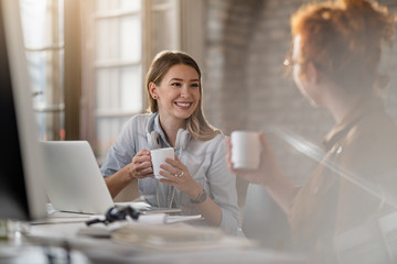 Happy businesswoman talking to her colleague while drinking coffee in the office.