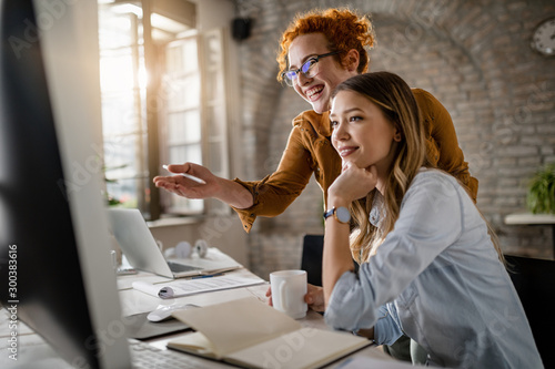 Fotomural Young happy businesswomen cooperating while using desktop PC in the office