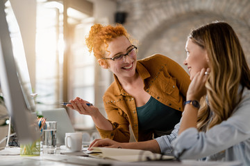 Happy female entrepreneurs communicating while working on a computer in the office.