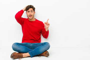 Wall Mural - young handsome man laughing, looking happy, positive and surprised, realizing a great idea pointing to lateral copy space sitting on the floor