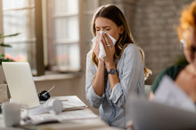 Young Businesswoman Using A Tissue While Sneezing In The Office.
