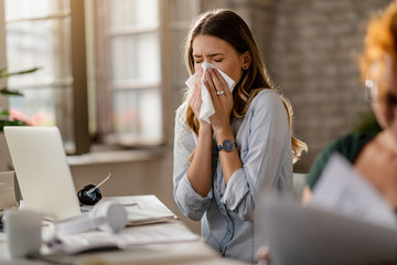 young businesswoman using a tissue while sneezing in the office.