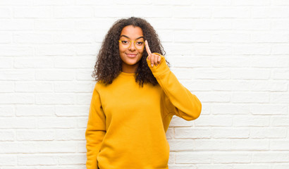 Wall Mural - young black woman smiling and looking friendly, showing number one or first with hand forward, counting down against brick wall